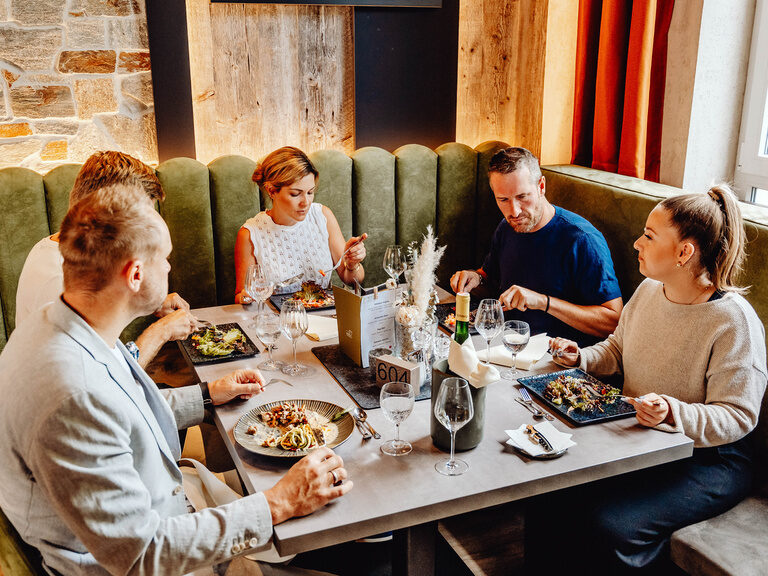Geselliges Beisammensein im Das Rudolf Restaurant Eine Gruppe von vier Personen sitzt in einem stilvollen Restaurant und genießt eine Mahlzeit.