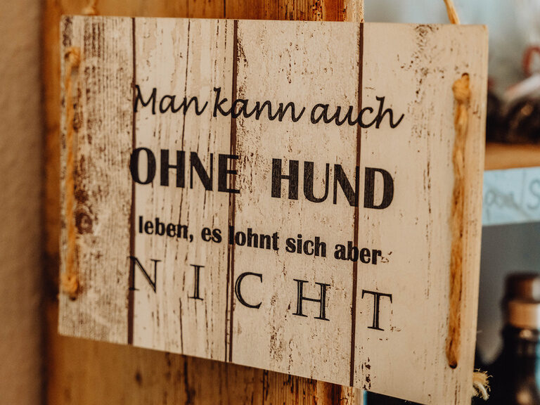 "Man kann ohne Hund leben, aber lohnt sich aber nicht" Ein Holzschild hängt neben einer Tür und trägt eine klare Botschaft.